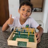 Menino mostrando o pebolim de palitos de picolé que construiu
