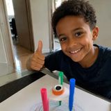 Menino sorrindo ao lado de um robô desenhista feito com canetinhas