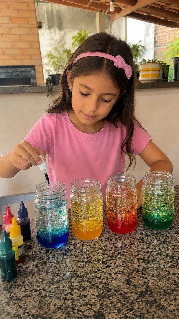 Menina pingando corante em potes de um experimento colorido